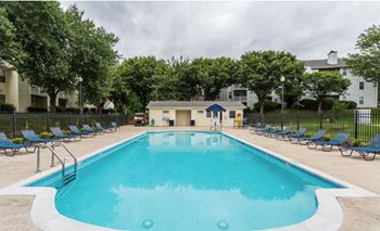 A swimming pool with chaise lounge chairs and an apartment building in the background